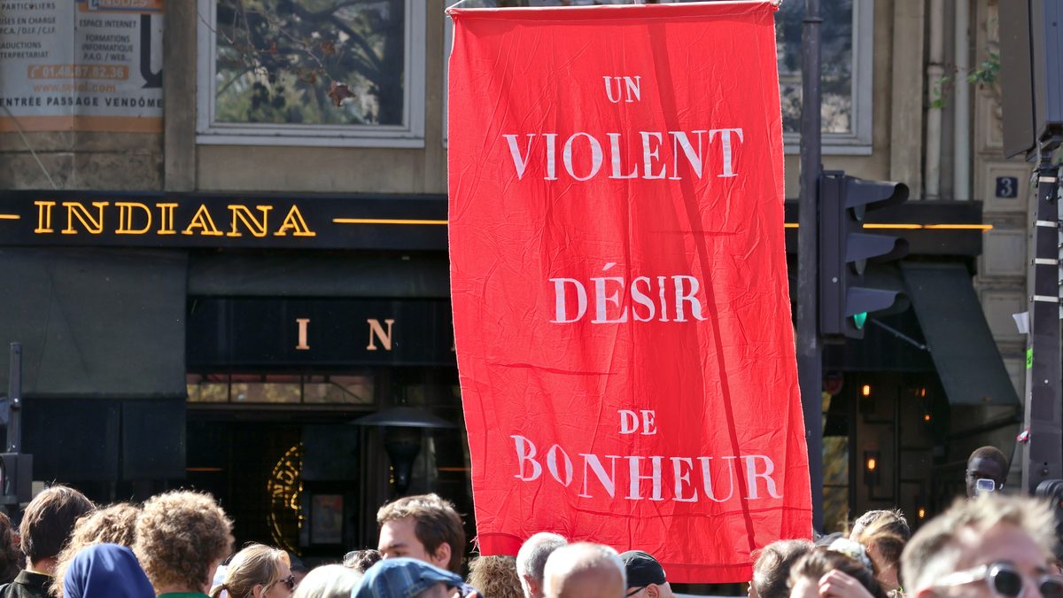 Faixa vermelha com a frase Un violent désir de bonheur sobre a multidão de estudantes em Paris.