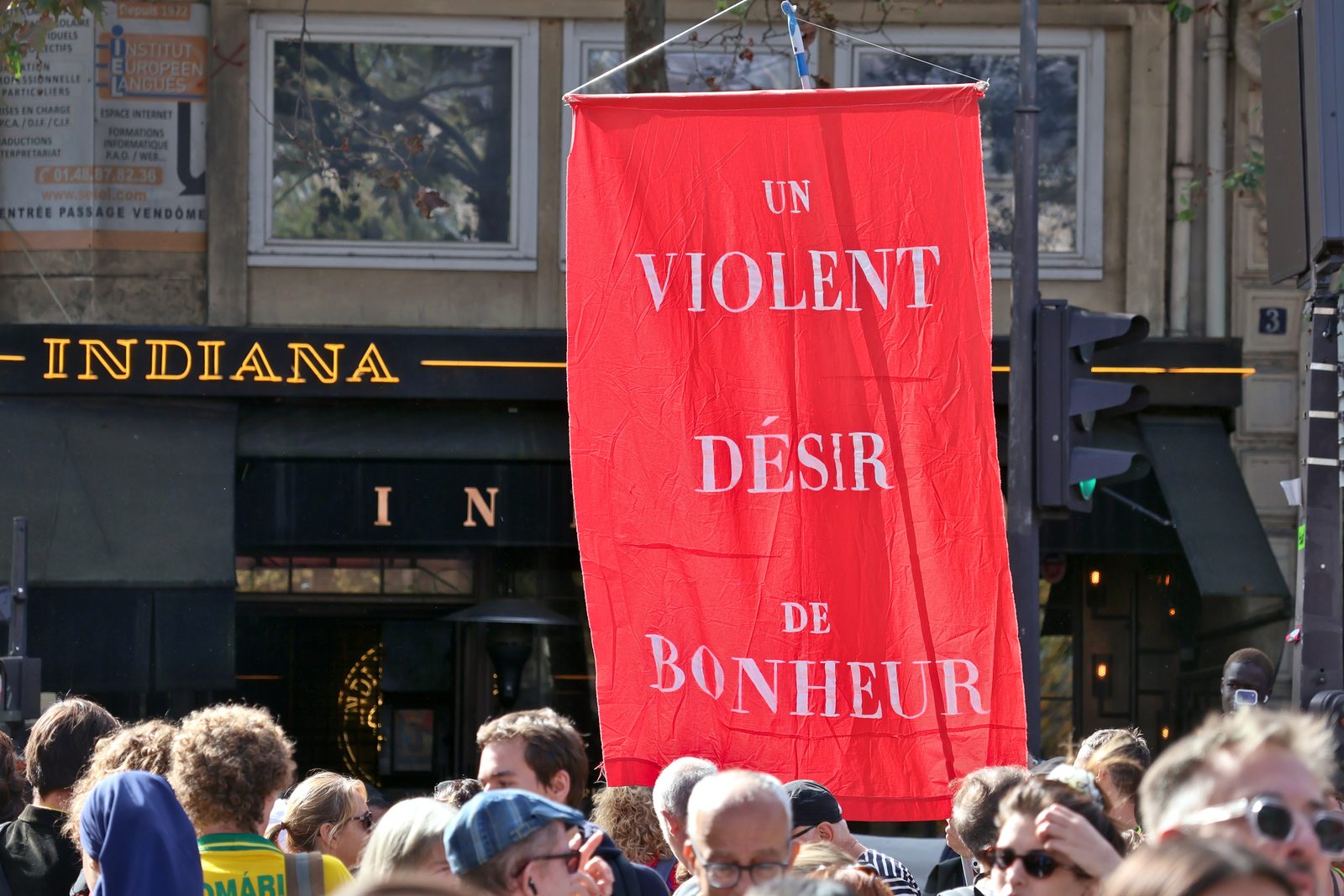 Faixa vermelha com a frase Un violent désir de bonheur erguida sobre a multidão de estudantes numa rua de Paris.